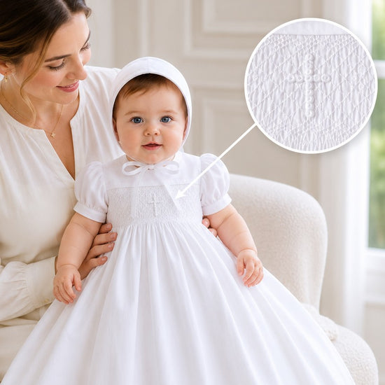Carriage Boutique white hand-smocked christening gown with cross detail and matching bonnet worn by an infant.