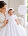 Carriage Boutique white hand-smocked christening gown with cross detail and matching bonnet worn by an infant.
