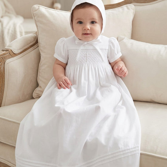 Carriage Boutique white hand-smocked christening gown with cross embroidery and matching bonnet on an infant.