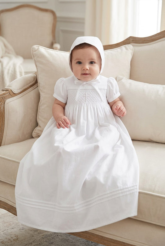 Carriage Boutique white hand-smocked christening gown with cross embroidery and matching bonnet on an infant.