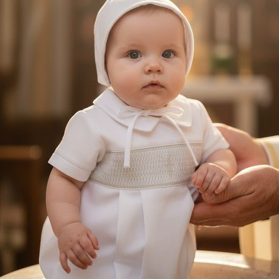 Carriage Boutique baby boy white christening bubble romper with smocked bodice and matching bonnet in a church setting