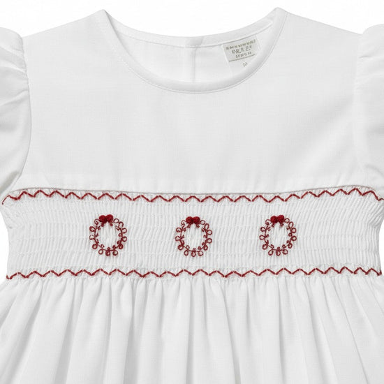 Carriage Boutique white toddler dress featuring hand smocking and red embroidered wreath details on the bodice