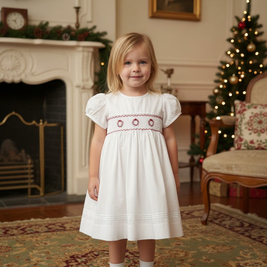 Toddler girl wearing a white Carriage Boutique dress with red smocked floral embroidery and puff sleeves
