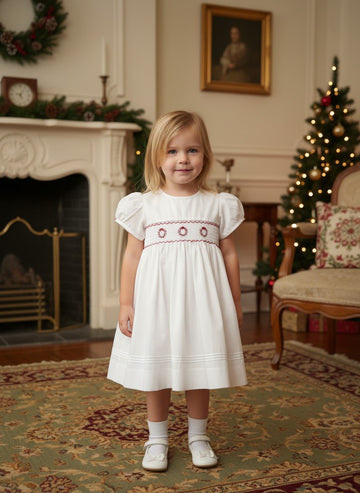 Toddler girl wearing a white Carriage Boutique dress with red smocked floral embroidery and puff sleeves