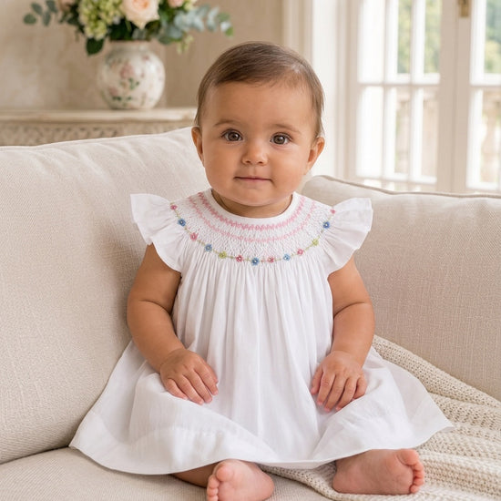 Carriage Boutique baby girl wearing a white vintage bishop dress with hand-smocked floral embroidery and flutter sleeves