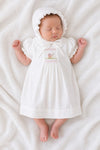 Carriage Boutique white heirloom baby dress with hand-smocking and pram embroidery, worn with a matching ruffled bonnet.