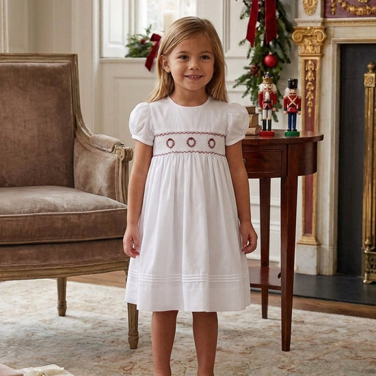 Carriage Boutique white toddler dress with red wreath embroidery and hand smocking, worn by a young girl at Christmas