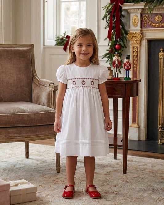 Carriage Boutique white toddler dress with red wreath embroidery and hand smocking, worn by a young girl at Christmas
