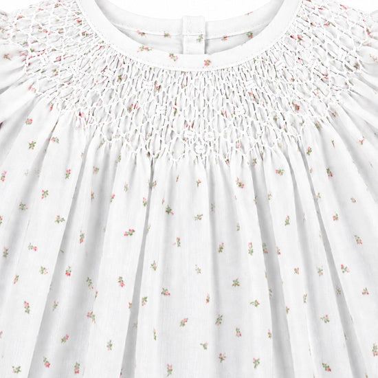 Carriage Boutique white newborn dress featuring delicate pink rosebud print and intricate hand-smocked bodice detail.