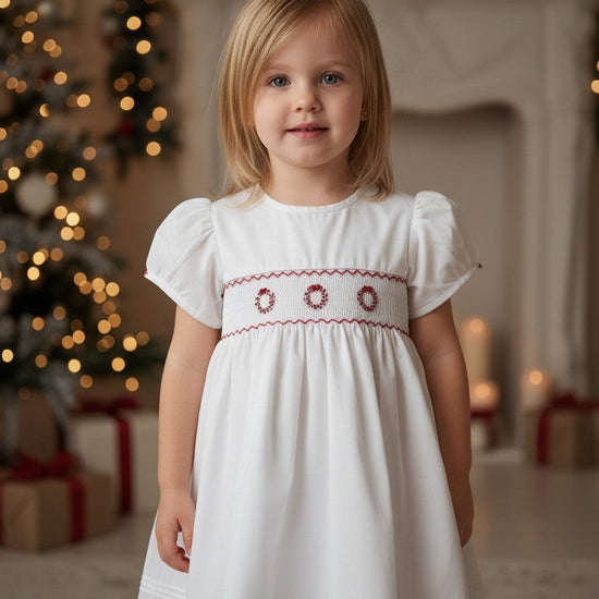 Toddler wearing a Carriage Boutique white short sleeve dress with red hand smocked wreath embroidery for holidays