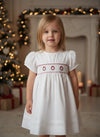 Toddler wearing a Carriage Boutique white short sleeve dress with red hand smocked wreath embroidery for holidays