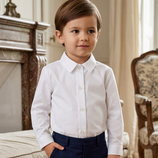 Carriage Boutique toddler boy wearing a crisp white long sleeve button-down shirt with navy trousers