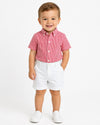 Toddler boy wearing Carriage Boutique white twill shorts and a red gingham shirt against a plain white background